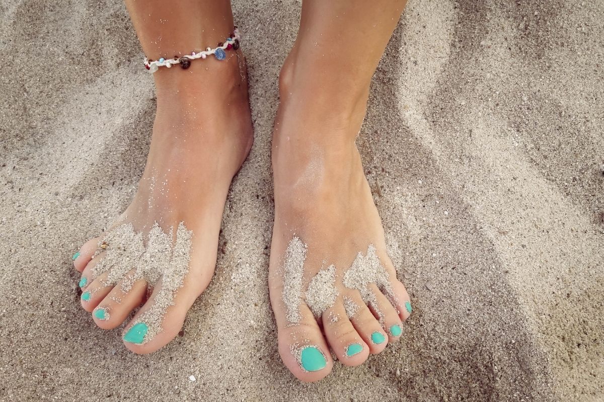 womans feet in beach sand with green toe nails